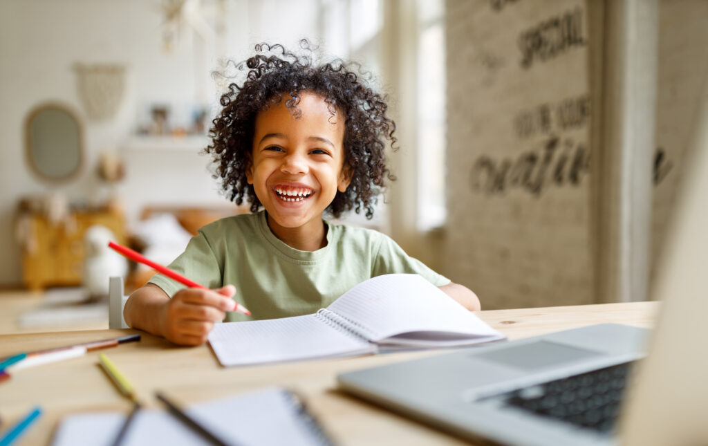 young boy with big hair smiling and writing in a notebook