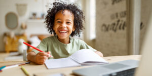 young boy with big hair smiling and writing in a notebook