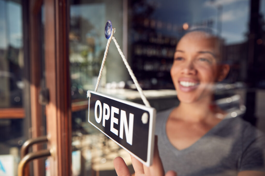 female shop owner hanging an open sign after getting the funds to start a small business