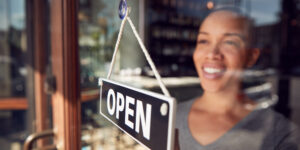 female shop owner hanging an open sign after getting the funds to start a small business