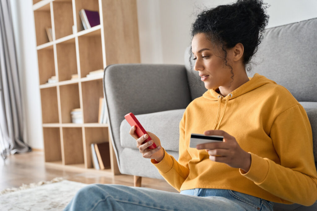 young woman sitting on the floor using her phone to see what kinds of credit cards can be used to build credit