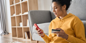 young woman sitting on the floor using her phone to see what kinds of credit cards can be used to build credit