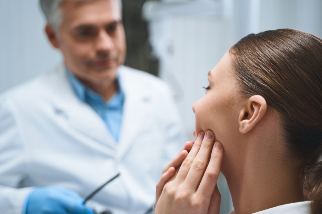 woman touching her mouth and asking her dentist about the best borrowing options for unexpected dental expenses