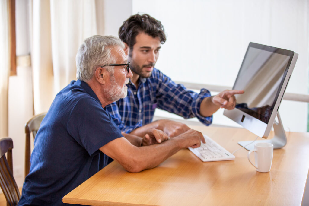 younger man pointing at the computer to show his father how to get the best loan for his needs