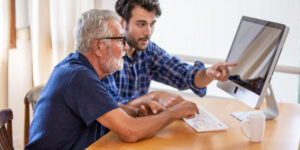 younger man pointing at the computer to show his father how to get the best loan for his needs