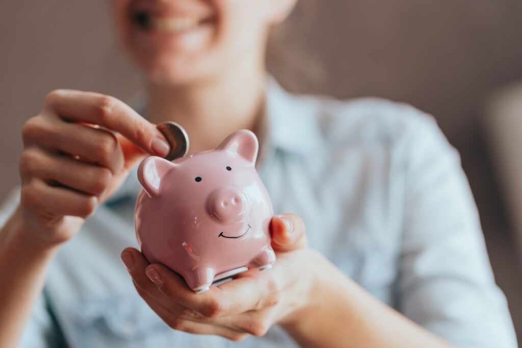 woman putting money in a piggy bank to illustrate 20 ways to save money on essentials