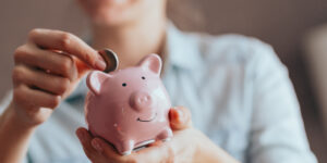 woman putting money in a piggy bank to illustrate 20 ways to save money on essentials