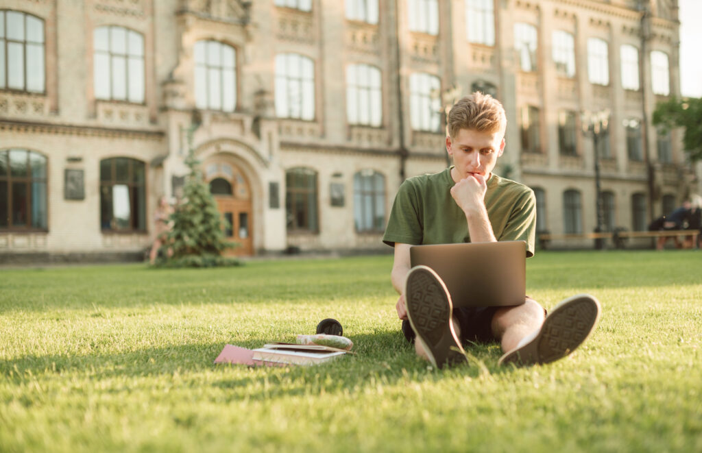 college student sitting on campus lawn worried that student loan debt collection scammers are calling his parents