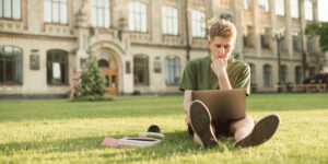 college student sitting on campus lawn worried that student loan debt collection scammers are calling his parents