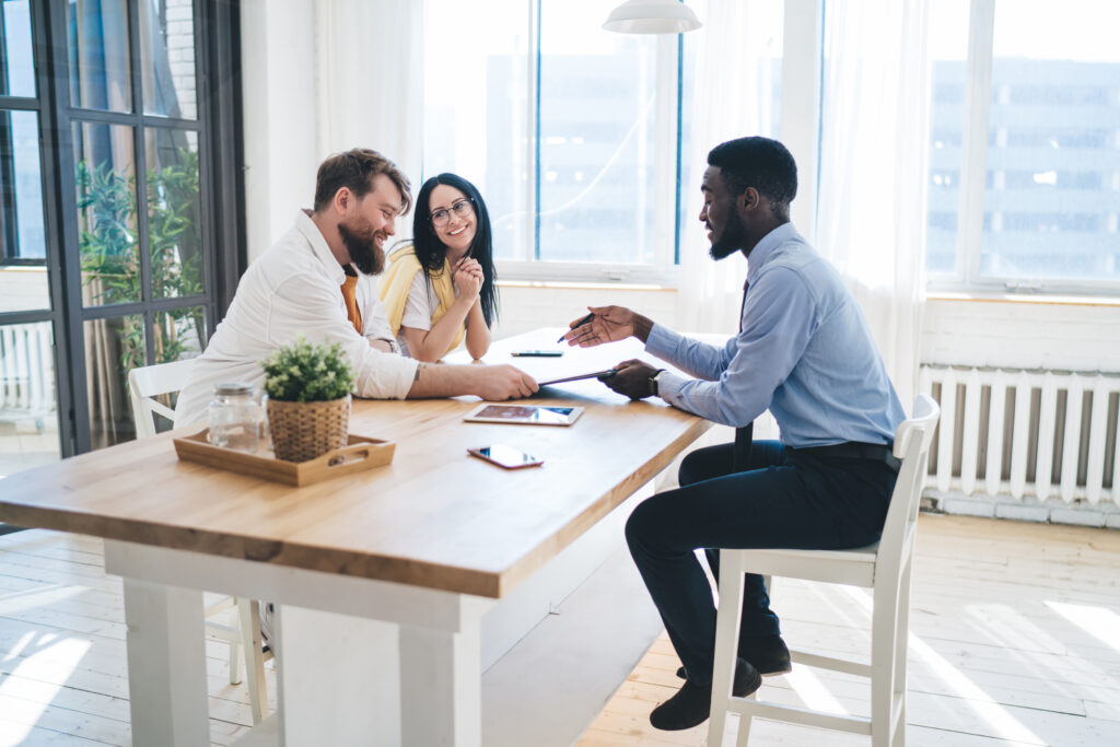 a young couple sitting at a table with an agent asking questions about renters insurance